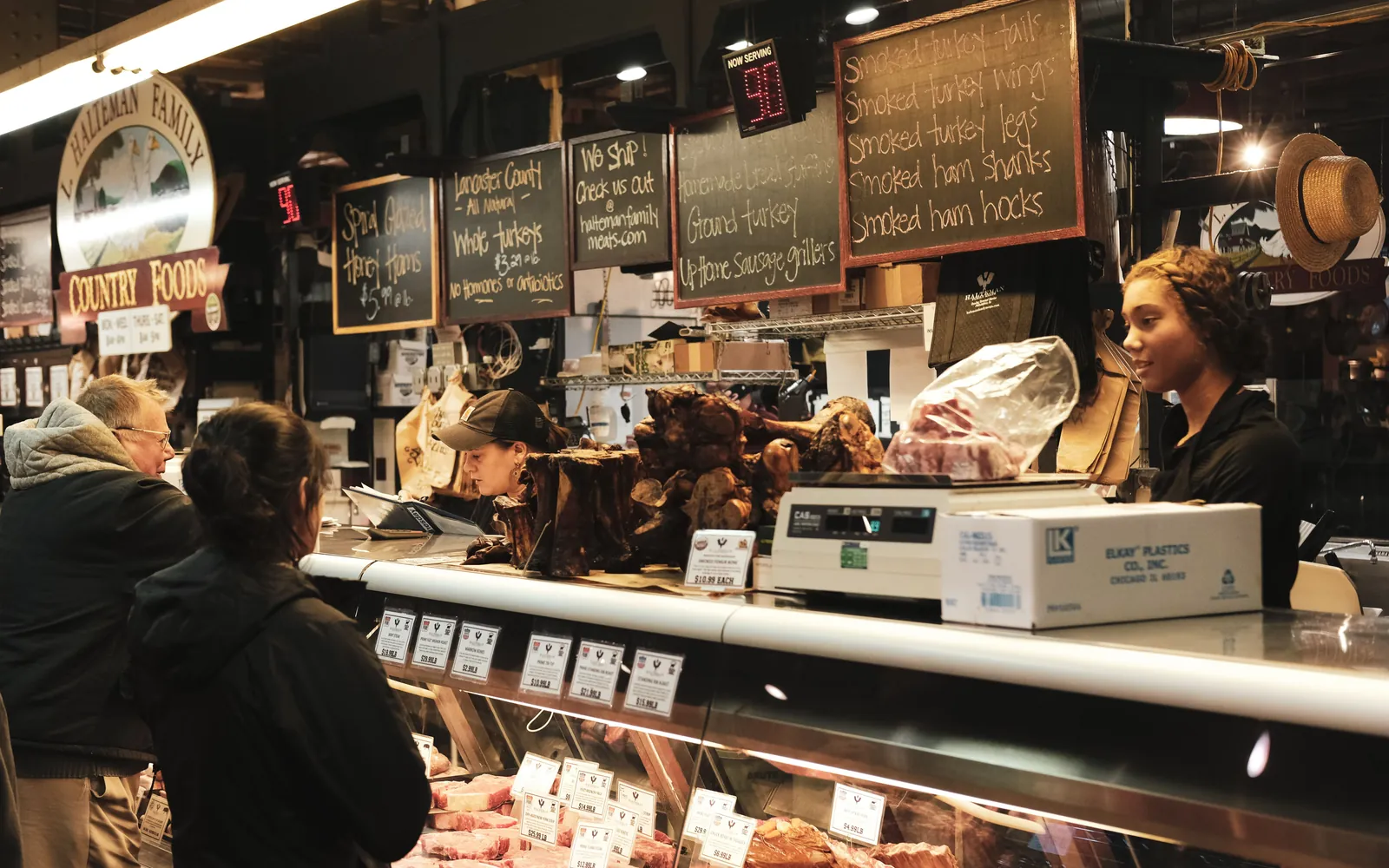 Employees serving customers at a busy meat counter.